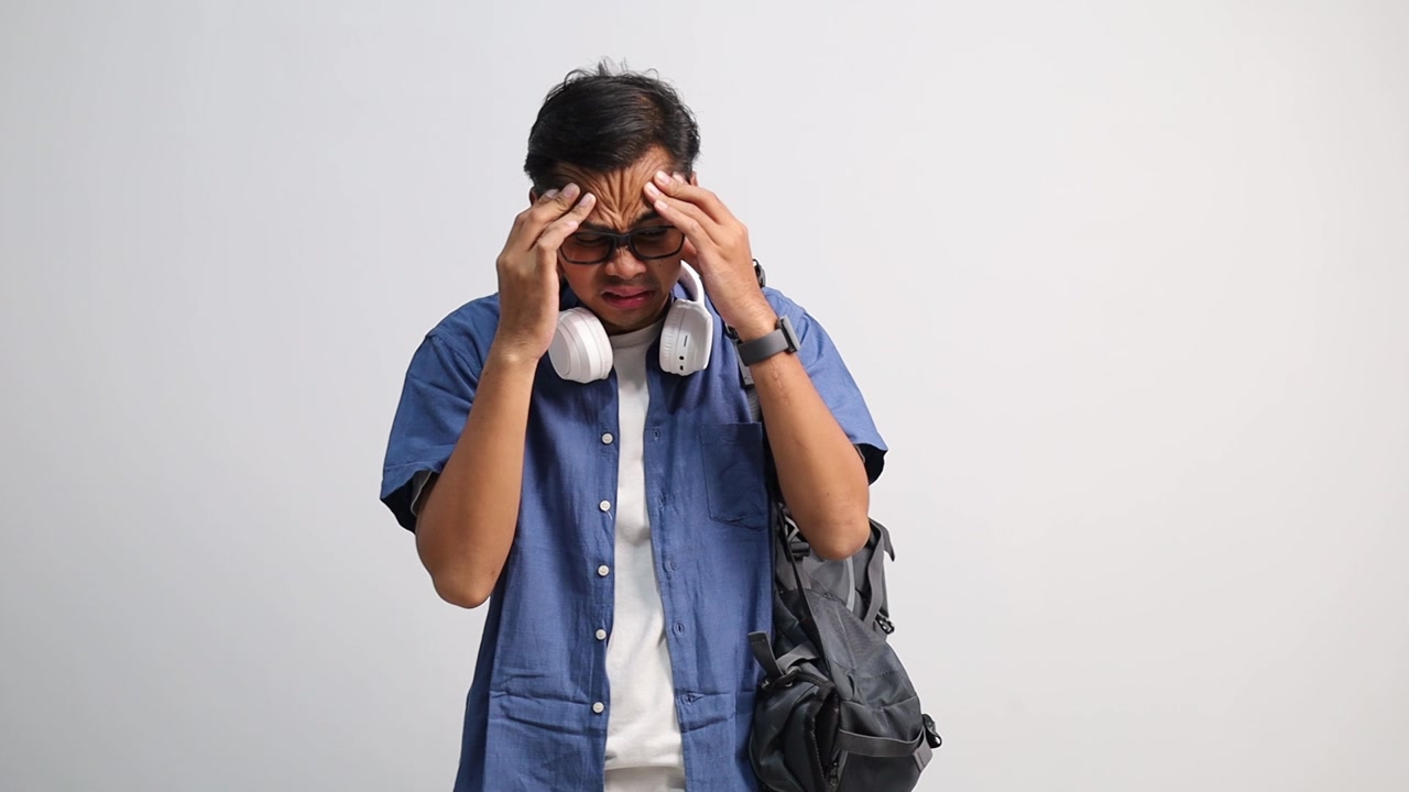 Young Asian student having headache and massaging temples to relieve the pain