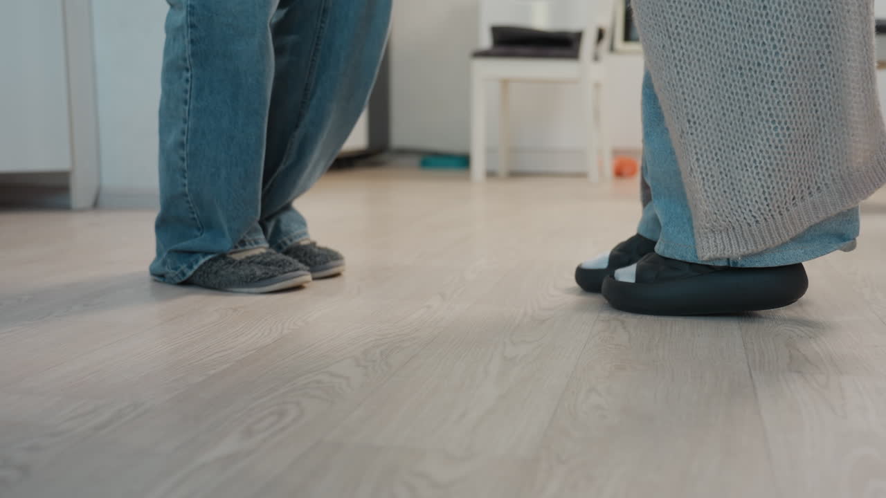 CloseUp Floor Feet Practicing Dance Steps In Living Room, Partners Taking Tentative Steps In Slippers And Denim, Playful Rehearsal With Balance Work And Shared Smiles, Home Choreography Session