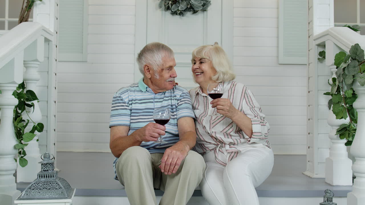 Senior elderly Caucasian couple drinking wine in porch at home, looking at camera and smiling