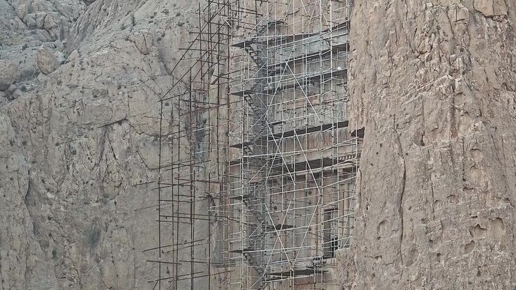 Scaffolding Surrounding Ancient Rock-Cut Tomb in Mountain Cliff