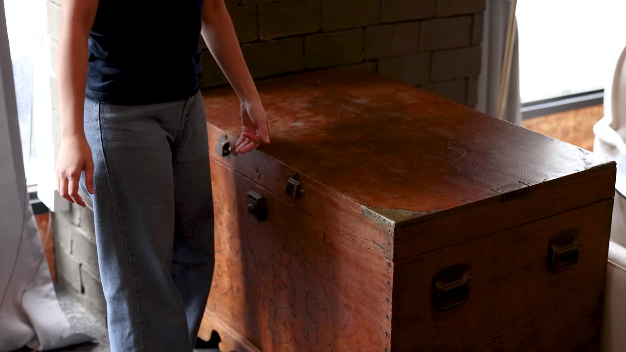 Individual closes large wooden storage chest in softly lit, rustic interior with steady camera movement