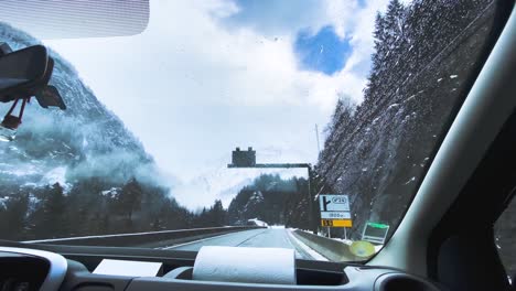 car driving on the snowy road to chamonix, france with wipers cleaning the windshield for safety - rolling shot