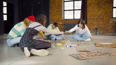 young environmental activists painting placards sitting on the floor