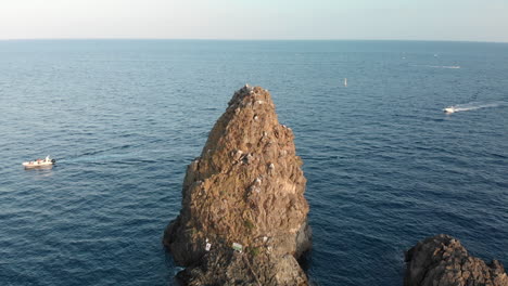 aerial poi, tall rocky island with steep sides, small boats nearby