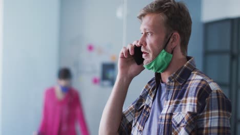hombre caucásico con máscara facial hablando en un teléfono inteligente en la oficina