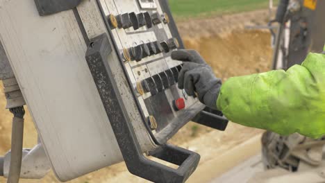 a construction worker in work clothes holds a hand on the knobs of control panel and controls the machine