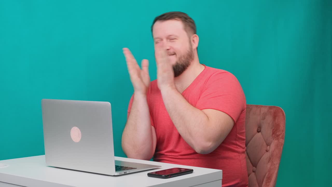 분홍색 티셔츠를 입은 행복한 청년 사업가는 노트북에서 일하며 녹색 화면에 손을 니다. 노트북을 바라보는 남성 이야기하는 남자의 초상화. 사무실에서 그의 책상에서 일하는 남자