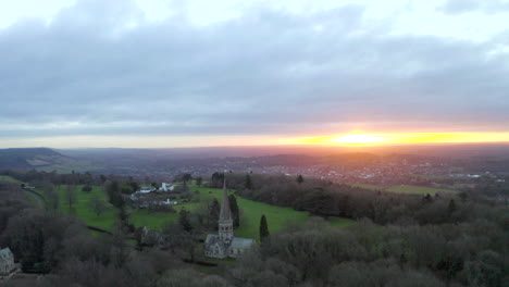 an aerial shot around an old english church on a hill in ranmore common, in dorking at sunrise