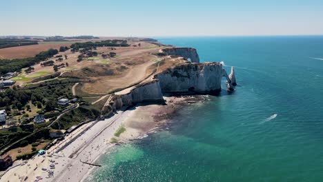 Aerial-flight-along-beautiful-coastline-of-Etretat-with-cliffs-consist-of-white-chalk-and-flint-during-sunny-day-in-France---Beautiful-blue-seascape-with-sandy-beach-and-tourists