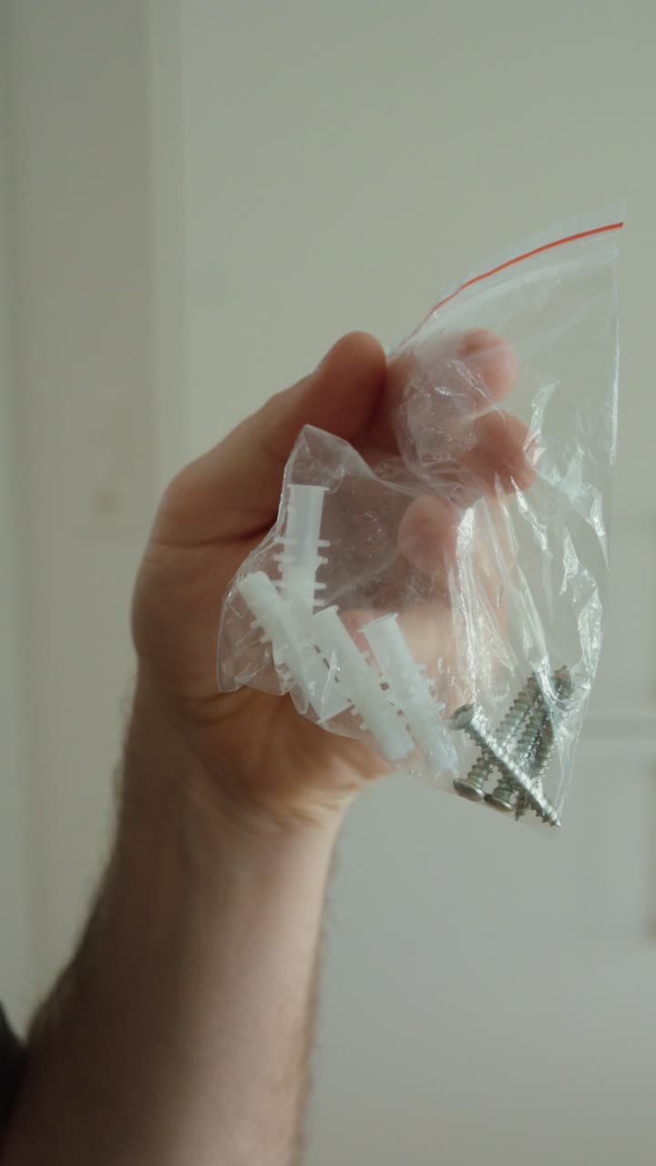 Primo piano di una mano che tiene viti e tasselli in un sacchetto di plastica, rappresentando riparazioni fai-da-te, miglioramenti domestici e lavori di costruzione