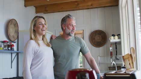 happy caucasian mature couple drinking coffee and looking through the window in the kitchen