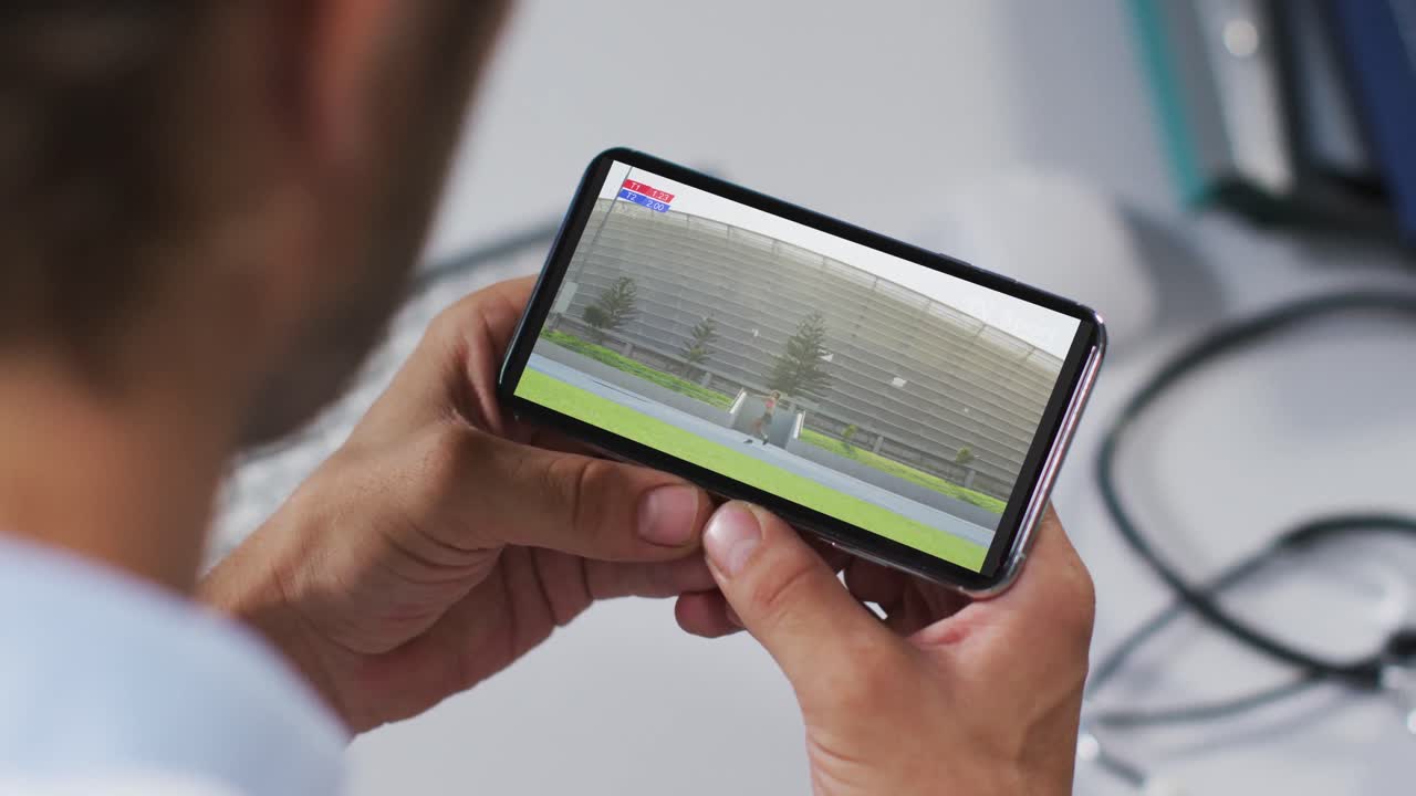 compuesto de un médico masculino viendo un evento de jabalina de atletismo en un teléfono inteligente