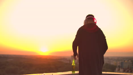 a man drinks beer standing on the roof and contemplates the world. look at the view of the city at sunset from a height. the roof of a skyscraper.