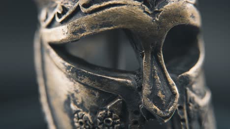 A-close-up-macro-professional-slow-pan-right-shot-of-a-spartan-face-design,-warrior-ancient-greek-bronze-helmet,-on-a-360-rotating-stand,-studio-lighting,-4K-smooth-movement