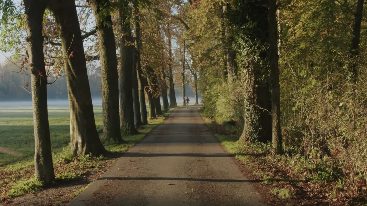 Un uomo corre su una strada in un parco durante una fredda mattina autunnale mentre il sole sorge