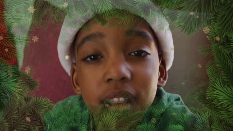 animation of fir tree and snowflakes over african american boy wearing santa hat