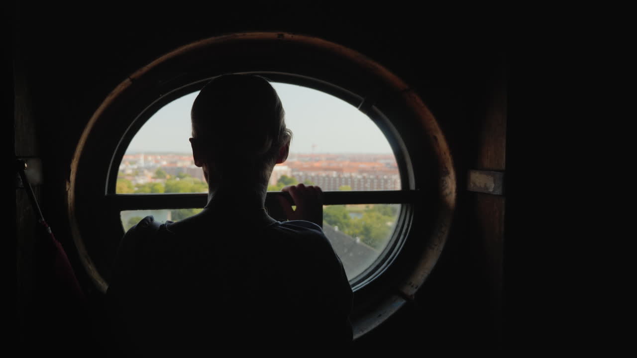 덴마크 코펜하겐 도시 옥상에 있는 둥근 창문을 바라보는 여성의 실루엣