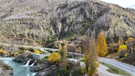 drone footage captures the vibrant autumn landscape of kawarau gorge, showcasing the river, trees, and surrounding hills in queenstown, new zealand