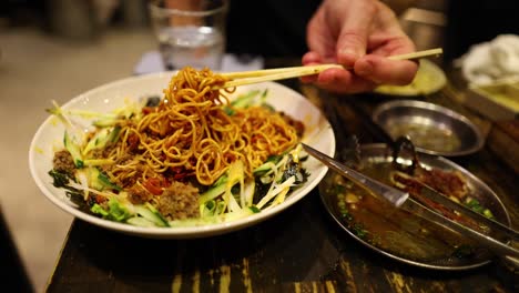 person eating noodles with chopsticks from a plate