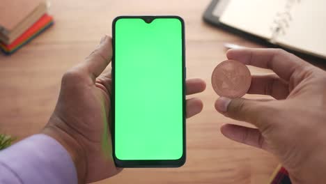 person holding a bitcoin coin and a phone with a green screen