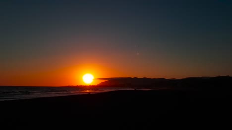 Slow-panning-shot-of-sunset-by-the-beach-with-lone-plane-contrail-in-the-sky-at-San-Buenaventura-State-Beach-in-Ventura,-California,-United-States