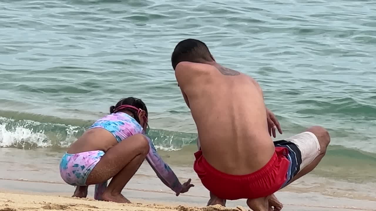 momento amoroso como padre filipino y hija hispana jugando en la arena en la playa, toma estática