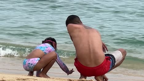 loving moment as filipino father and hispanic daughter play in the sand on the beach, static shot