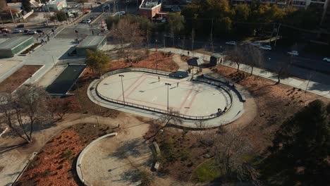 Aerial-orbit-of-people-enjoying-in-skate-rink-in-autumnal-public-park-in-Los-Dominicos,-Santiago,-Chile