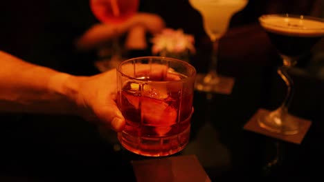 hand swirling a negroni cocktail in a bar