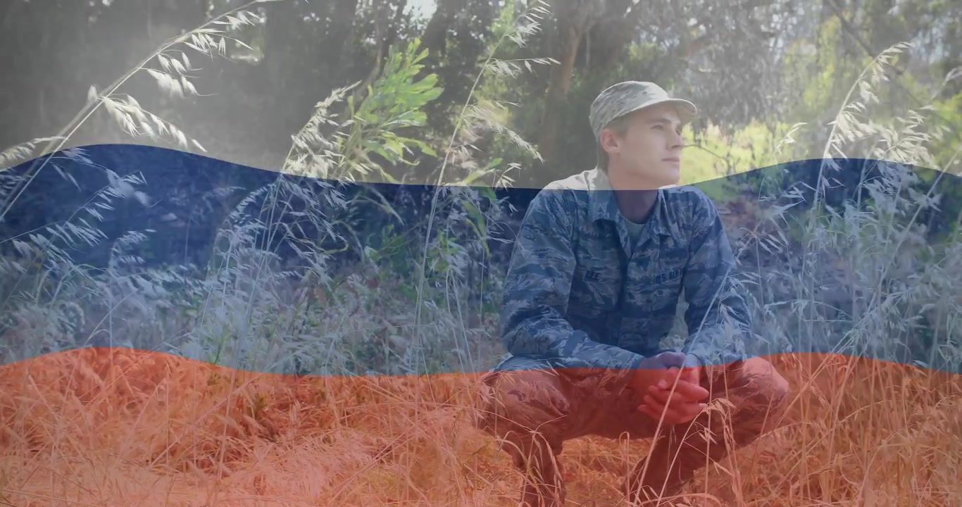 Militærmand i camouflagedragt sidder i græsset, trefarvet overlay afslører ham, mens han scanner området.