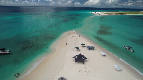 aerial zoom in cayo de agua island, people enjoy day beach, white sand, boats and beach umbrellas