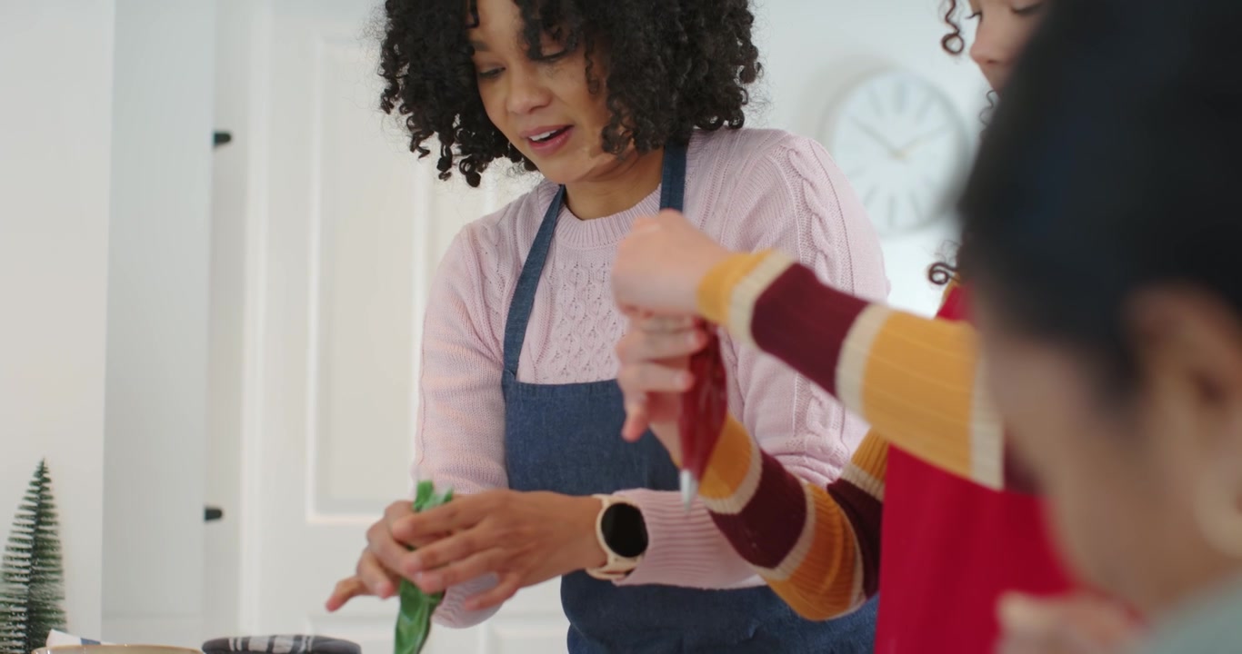 Hands twisting green piping bag, African American females piping icing on cooling rack at kitchen