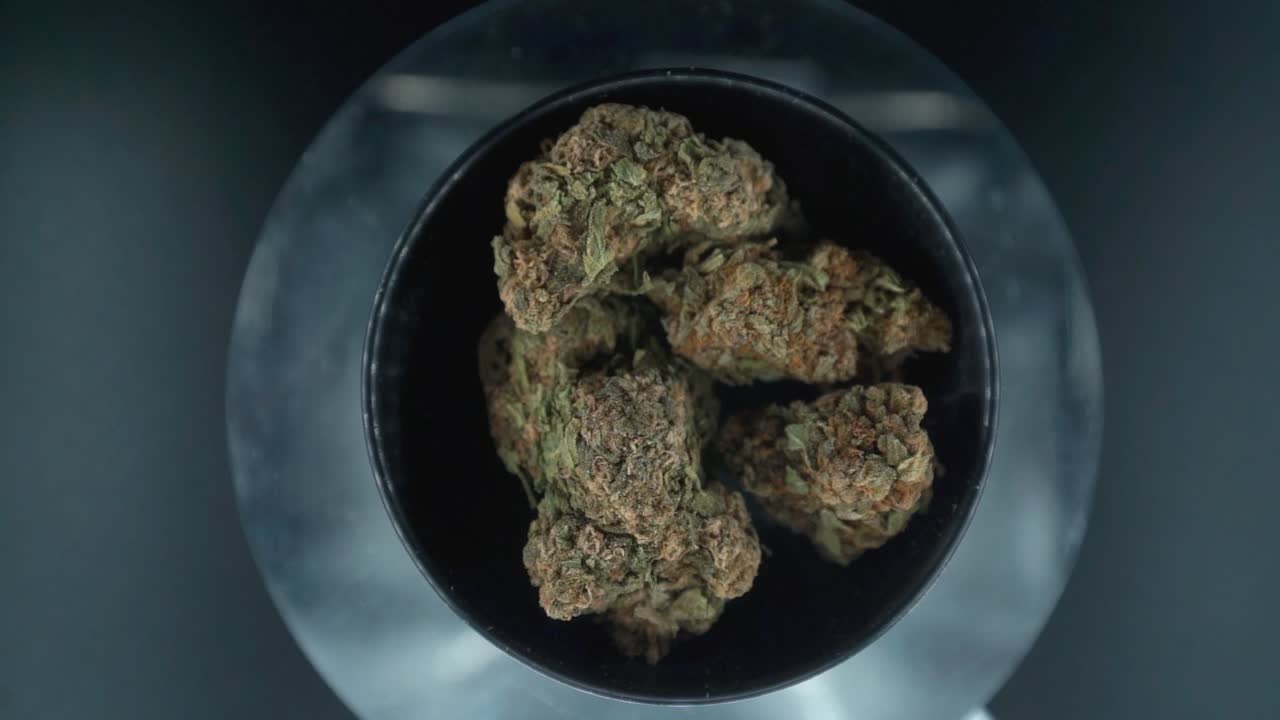 Grayish Green Dried Marijuana Buds view from above Shot, pile of dried marijuana plants in a shiny bowl, trichomes strains, on a reflecting rotating stand, studio lights, slow motion 120 fps
