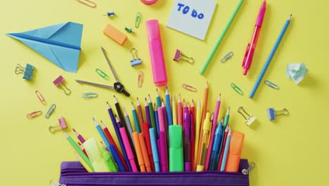 Video-of-school-supplies-and-notebooks,-paper-clips,-pens-over-yellow-background