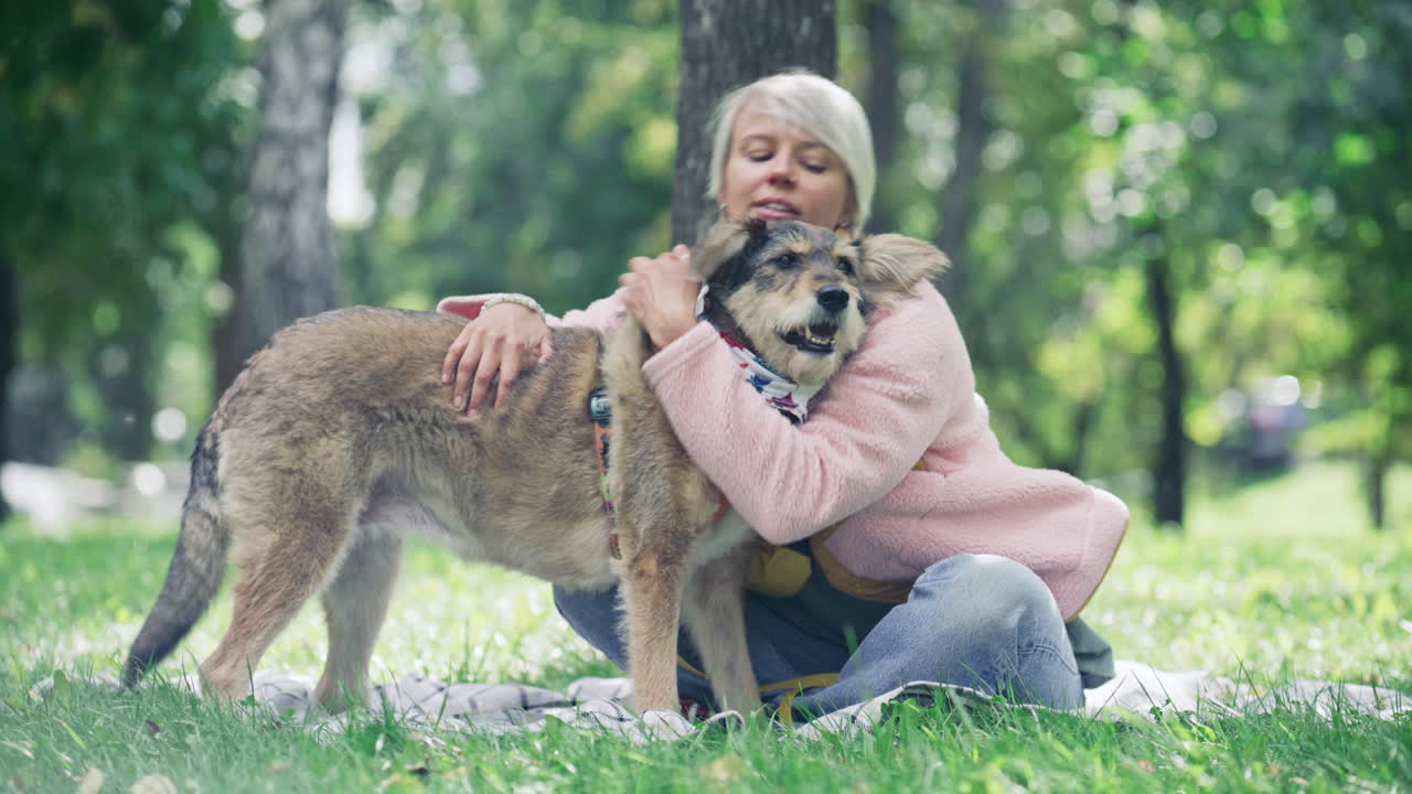 Woman Petting and Hugging Dog while Sitting in Lush Green Park