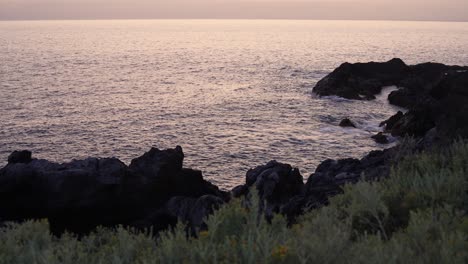 Seascape-view-with-large-rocks-from-the-highlands-during-sunset-with-grass-in-the-foreground,-static-slow-motion