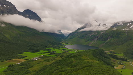 stunning nordic valley with low hanging clouds and alpine lake by farm plots