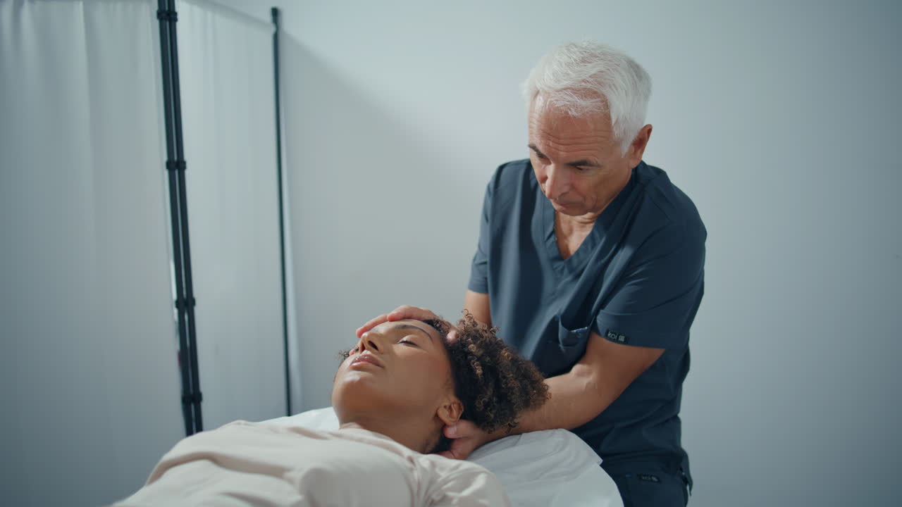 Physiotherapist touch patient head in clinic ward. Mature professional pressing