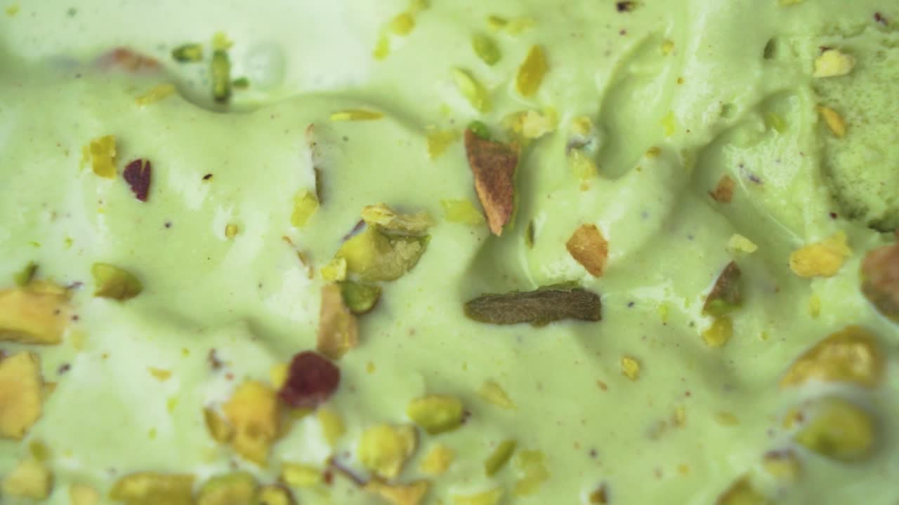 Close-up top-down shot of a creamy pistachio ice cream scoop with scattered raw nuts for texture