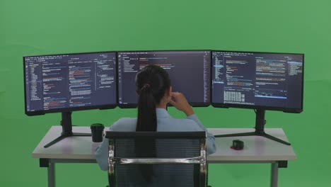 back view of asian woman developer thinking about something while write code with multiple computer screens in green screen studio