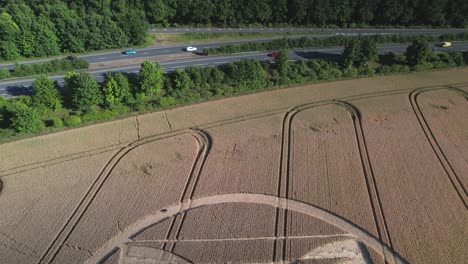 Filmische-Luftaufnahmen-Von-Kornkreisen-In-Einem-Feld-Mit-Gelbem-Korn,-Aufgenommen-Von-Einer-Drohne-In-Der-Britischen-Micheldever-Station-Mit-Fahrenden-Autos-In-Der-Nähe