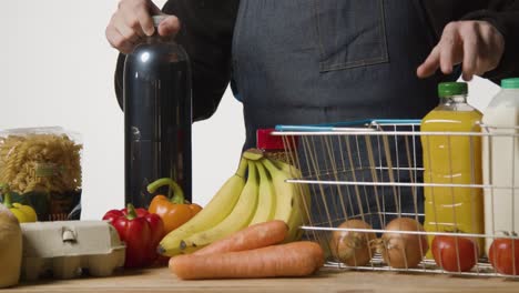 foto de estudio de un trabajador de la tienda en la caja sacando alimentos básicos de la cesta de la compra de alambre del supermercado