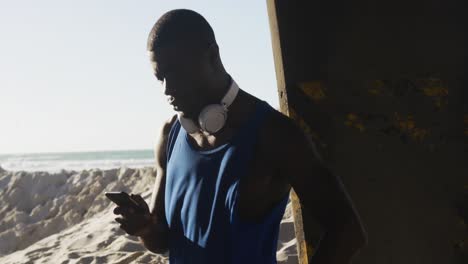 Afroamerikanischer-Mann,-Der-Sein-Smartphone-überprüft-Und-Während-Des-Trainings-Im-Freien-Am-Meer-Eine-Pause-Macht