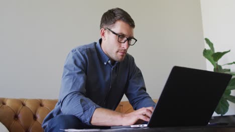 hombre caucásico con gafas trabajando desde casa usando computadora portátil