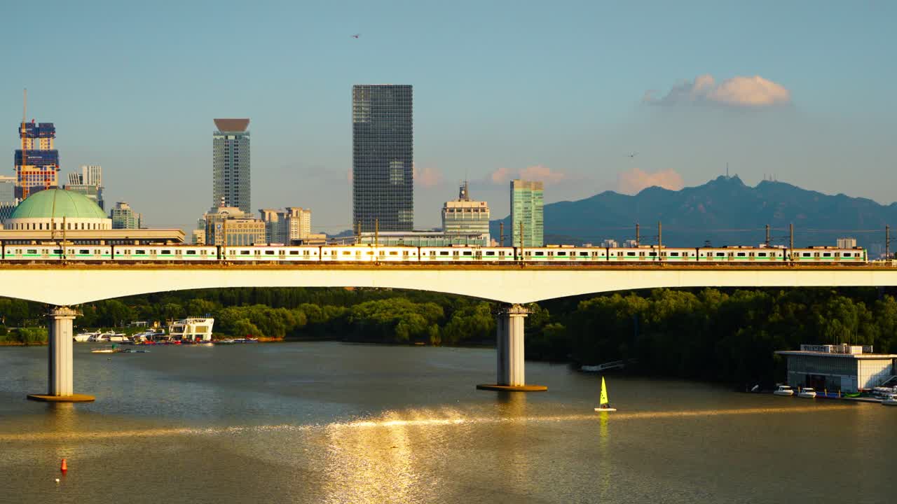 Seoul Line 2 subway train crosses Dangsan Railway Bridge over Han River with golden sunset light reflecting on its windows and Yeouido skyscrapers in background