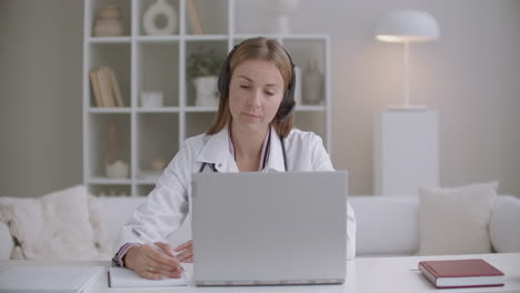 online appointment with doctor female therapist is asking patient by videocall on laptop and writing notes in copybook