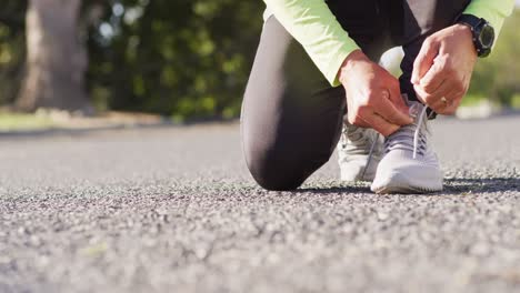 video of low section of senior biracial man in sports clothes kneeling on street tying shoelaces