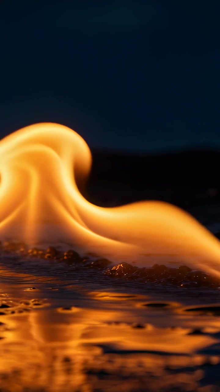 Vertical video: Rising flame wave moving across wet surface at night, casting golden reflections