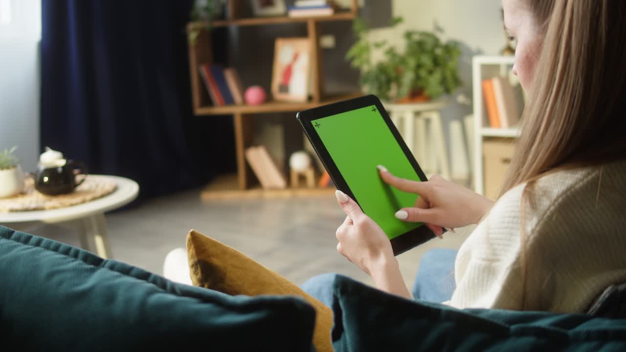 mujer usando una tableta de gadget con pantalla verde. persona femenina irreconocible deslizando la llave de croma, sentada en el sofá en la sala de estar. compras en línea, navegar por internet. tiempo libre en casa, ocio