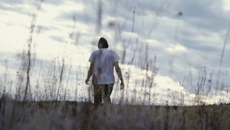 man walking away from camera towards sunset through tall grass, slow motion